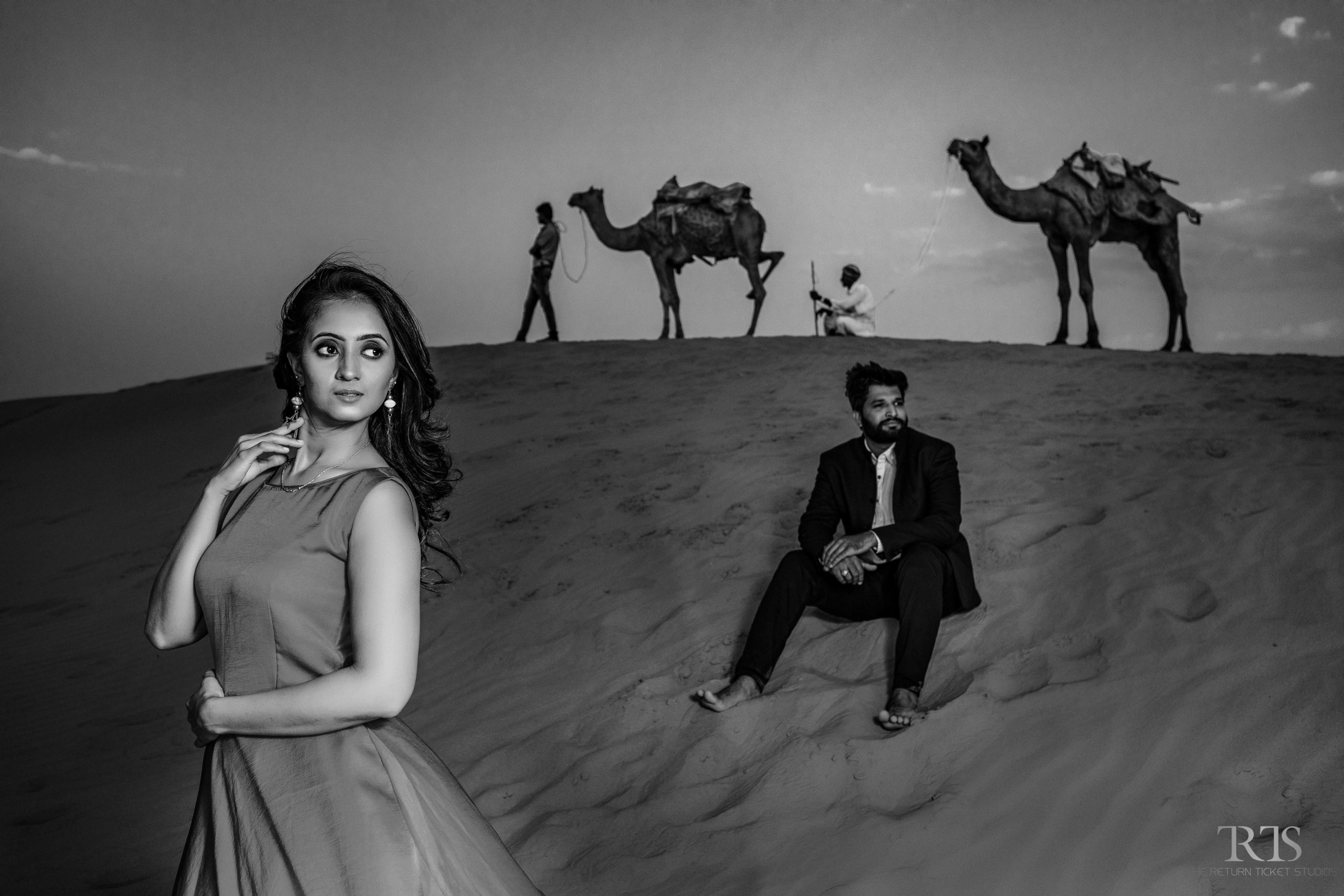 couple shot in the desert with camels in the behind Beautiful candid photography of pre wedding and wedding by The Return Ticket Studios 