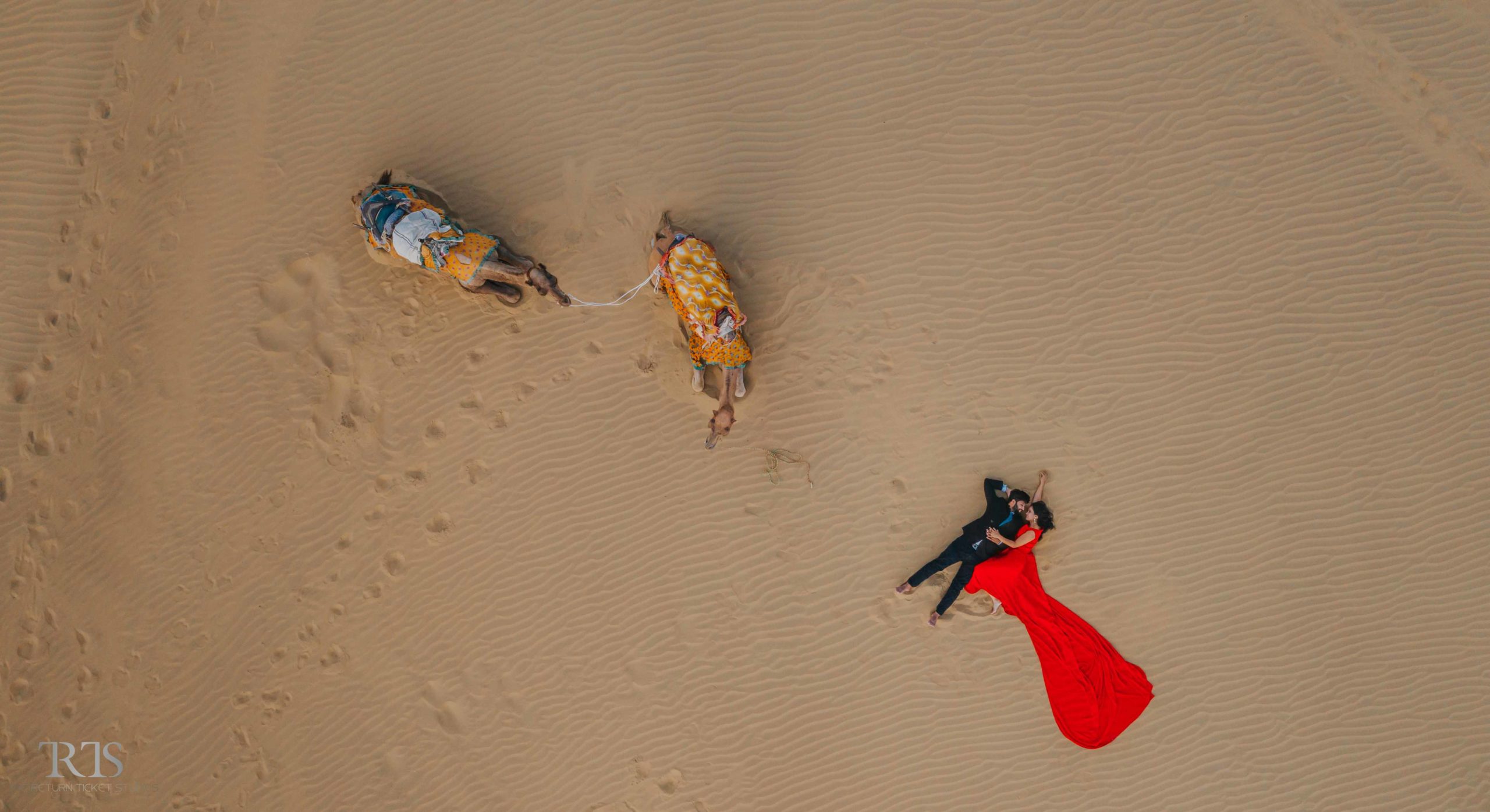 beautiful aerial/drone shot of couple in the desert in the long dress with camel Beautiful candid photography of pre wedding and wedding by The Return Ticket Studios 