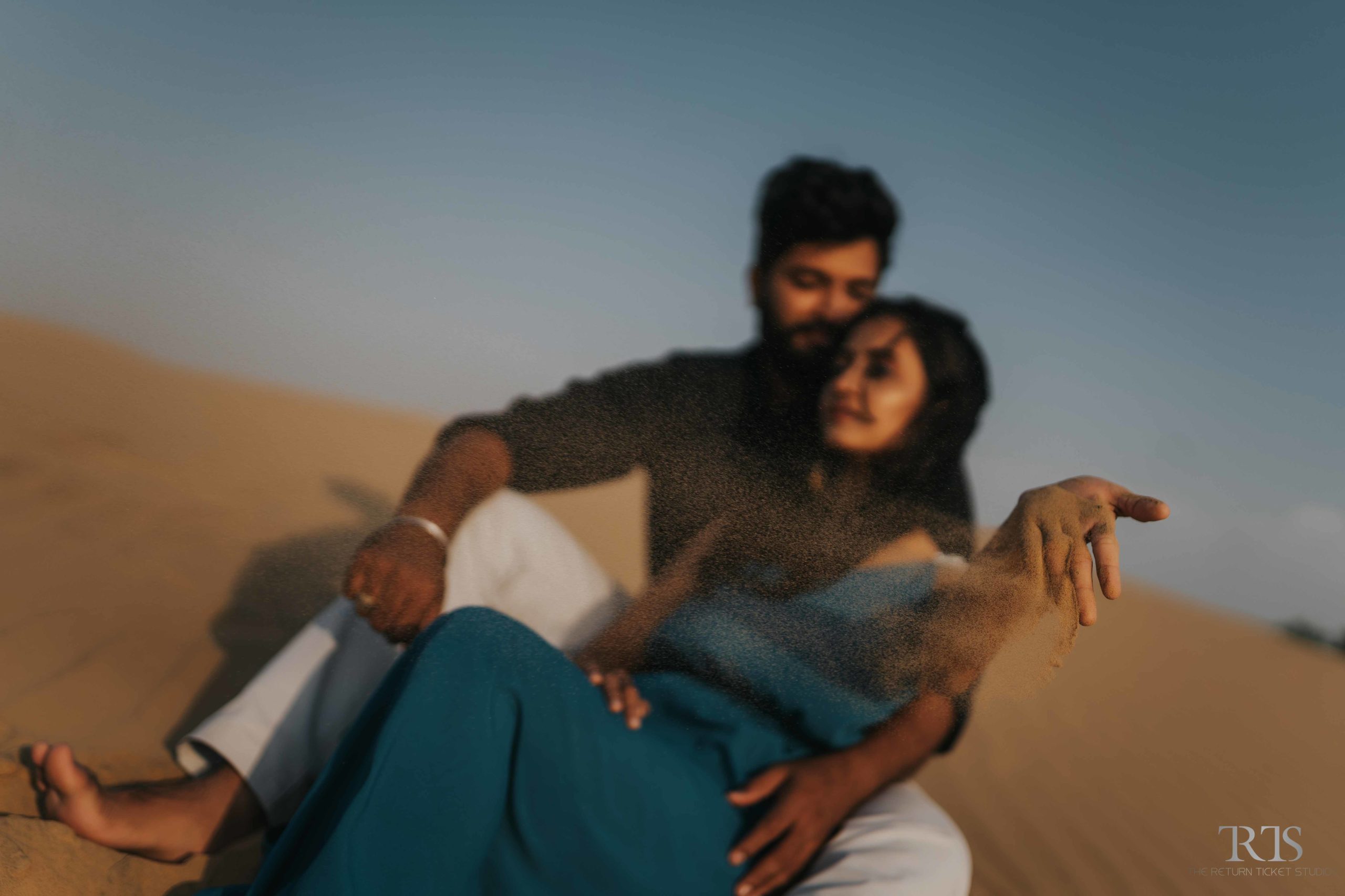 couple sitting in the desert wearing blue ress Beautiful candid photography of pre wedding and wedding by The Return Ticket Studios 