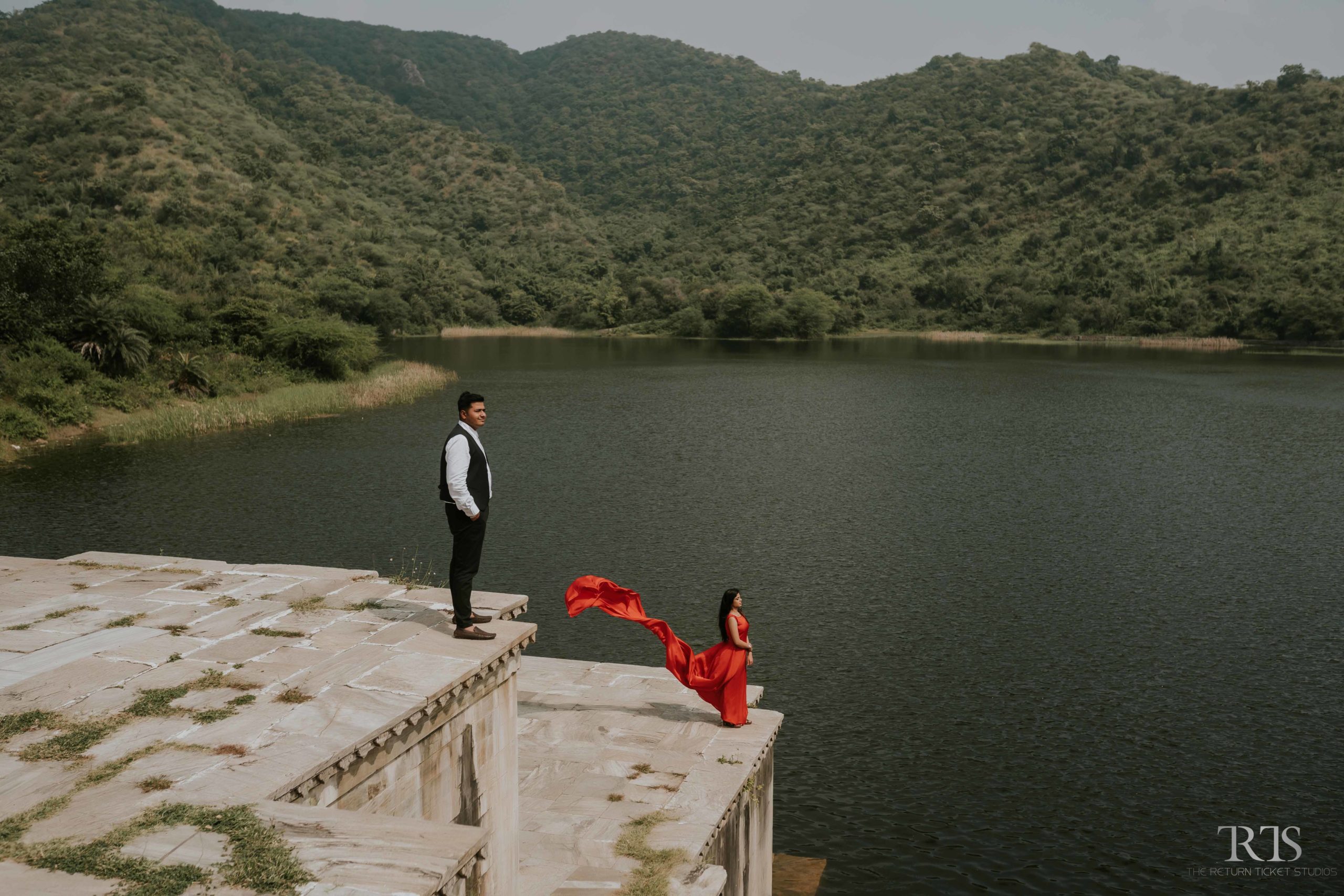 couple near by lake girl wearing red dress and boy in black suit